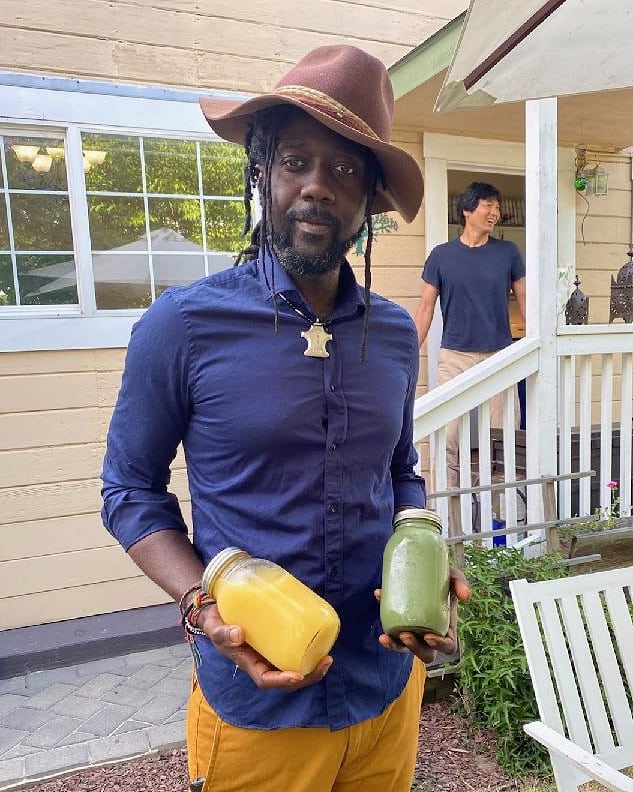 AshEL holding two jars of fresh green and golden juice outdoors